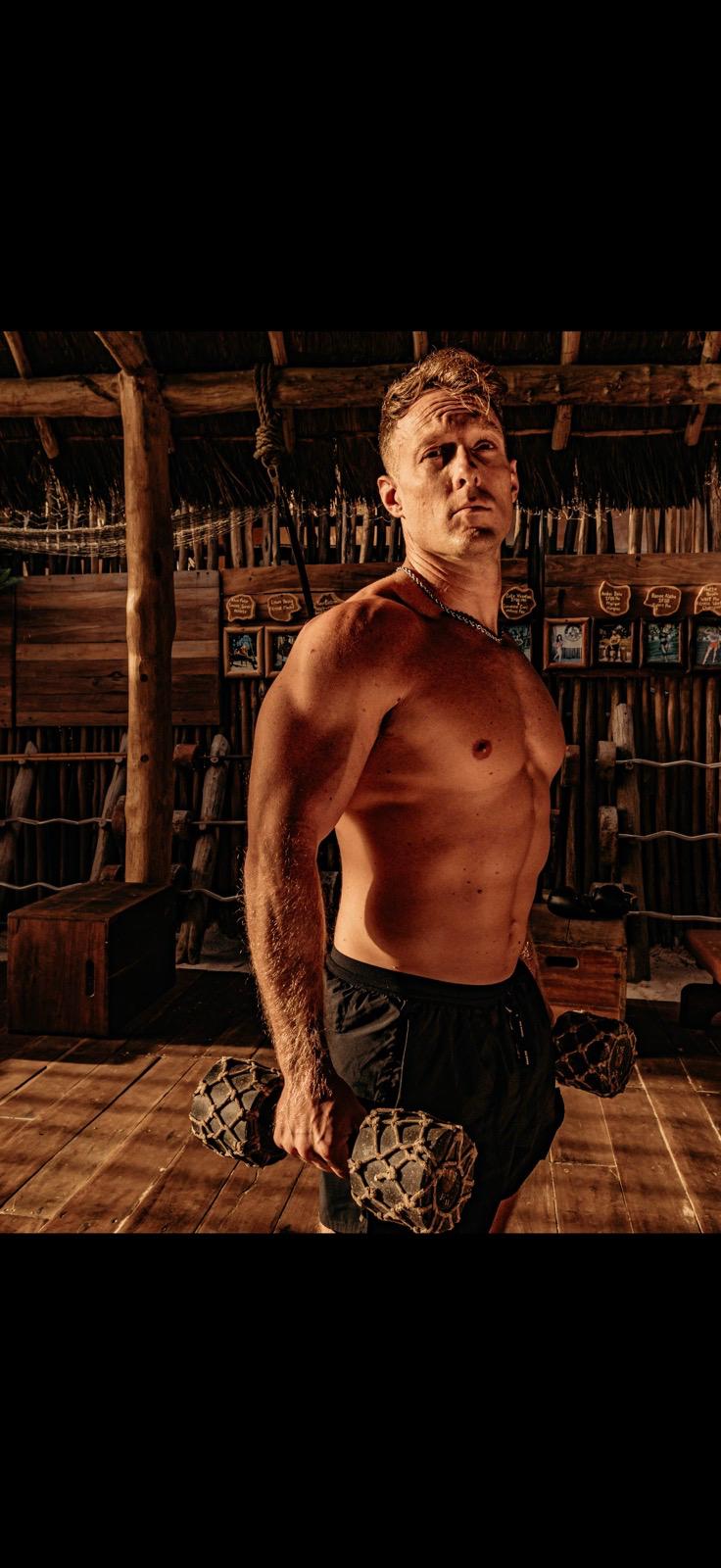 Mike Zdonczik holding rope-wrapped dumbbells under a palapa